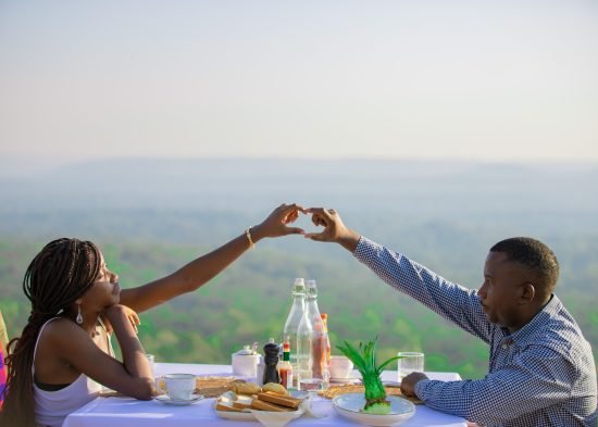 Couple enjoying a romantic sunset dinner at Entikko Safari Lodge, making a heart shape with their hands.