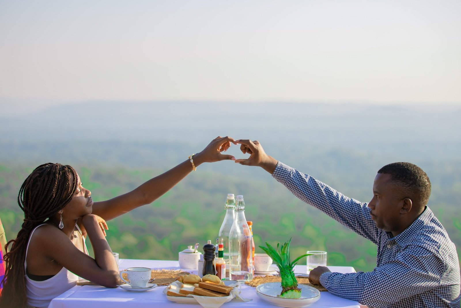 Couple enjoying a romantic sunset dinner at Entikko Safari Lodge, making a heart shape with their hands.
