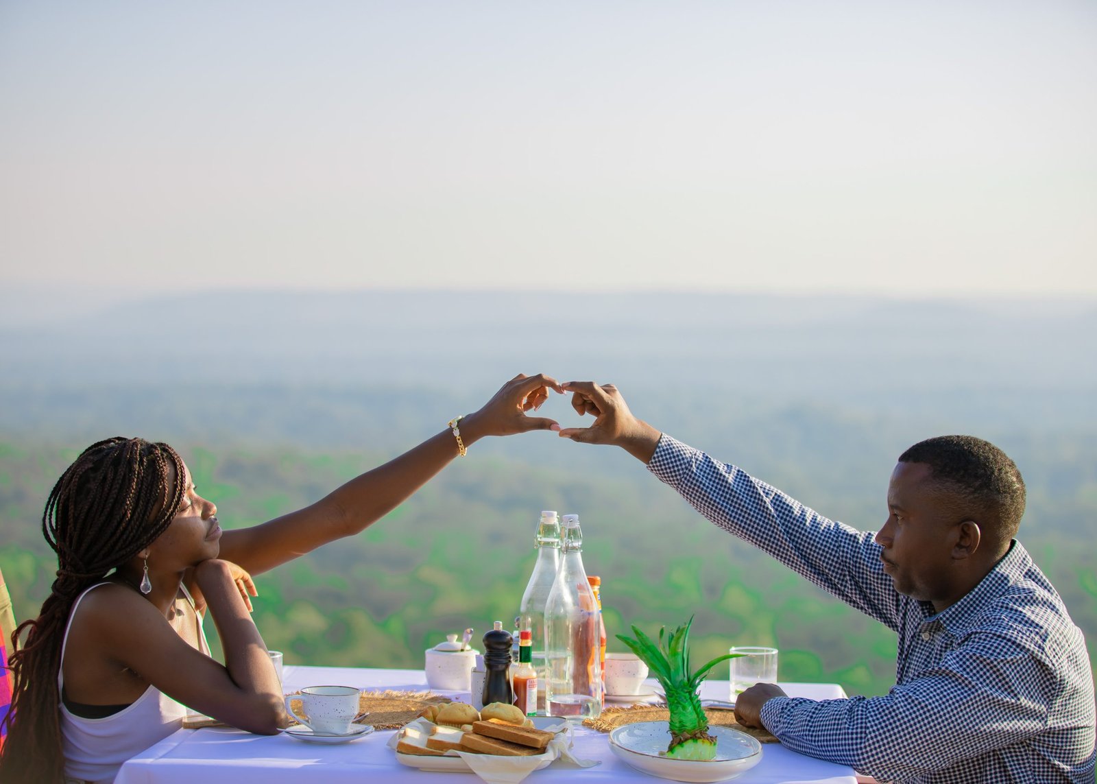 Couple enjoying a romantic sunset dinner at Entikko Safari Lodge, making a heart shape with their hands.