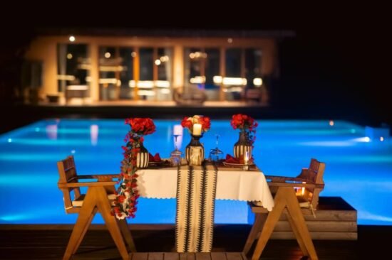 Romantic poolside dinner setup at night with glowing blue pool and candlelit table at Entikko Safari Lodge near Murchison Falls Uganda