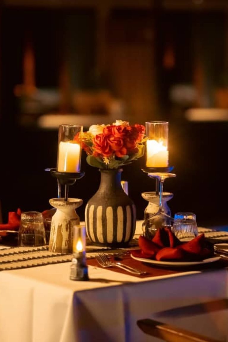 Romantic candlelit private dinner table with red floral centerpiece and striped runner at Entikko Safari Lodge Uganda